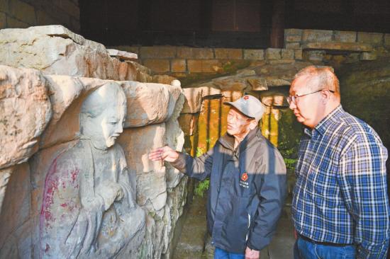 　　义务文保员（左）在向大足石刻研究院工作人员介绍普圣庙摩崖造像保护情况。